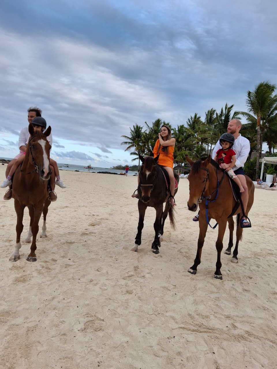 Guests including young children on horseback on a white sand beach
