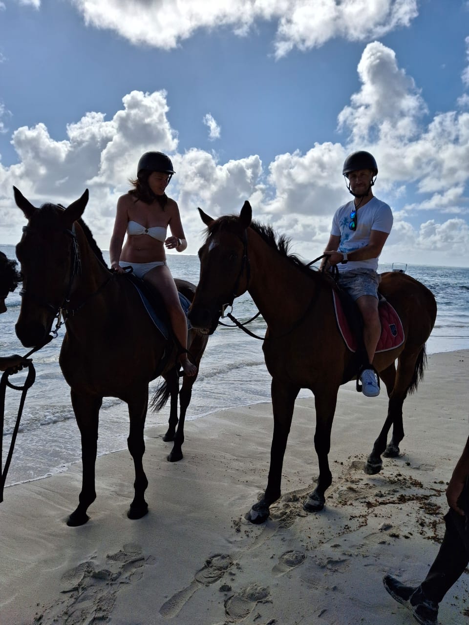 A couple wearing riding helmets on horses by the ocean in Mauritius